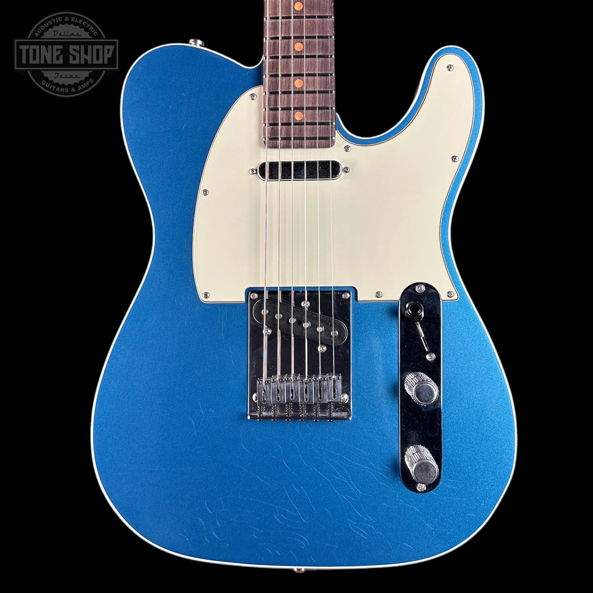 Blue electric guitar with a white pickguard on a black background, featuring the Tone Shop logo.