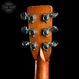 Close-up of the headstock of a wooden six-string acoustic guitar, showing six tuning pegs with 'MAGNA-TUSK' branding, on a solid black background.