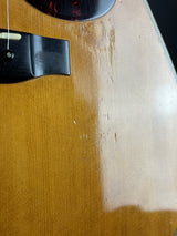 Close-up of a wooden acoustic guitar body showing the natural wood grain, a glossy finish, and part of the black bridge and sound hole surround.