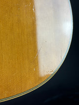 Close-up of a guitar body showing the natural wood grain finish and part of the decorative inlay border against a dark background.