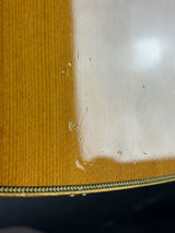 Close-up of a guitar body showing the natural wood grain top, a glossy white back panel, and a decorative black and gold binding edge.