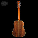 The back of an acoustic guitar with a rich dark brown wood grain finish, shown against a solid black background with a Tone Shop watermark in the top left corner.