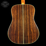 The back of an acoustic guitar made of rich, dark brown wood with a prominent vertical grain pattern and a gold-colored binding edge, shown against a solid black background.