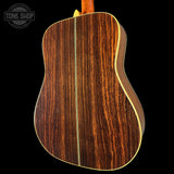 The back of an acoustic guitar with a rich dark brown wood grain finish, featuring a light-colored binding edge, shown against a solid black background with a Tone Shop watermark in the top left corner.