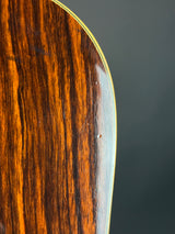 Close-up of a glossy dark brown wooden guitar body showing the wood grain and a light-colored edge trim against a dark gray background.