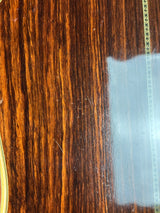 Close-up of a glossy dark brown wood grain surface with a decorative inlay line near the top and a small portion of a gold-toned rim visible at the bottom edge.