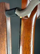Close-up of a polished reddish-brown wooden rifle stock with a black ribbed stock rest support and a gray sling, set against a dark gray background.