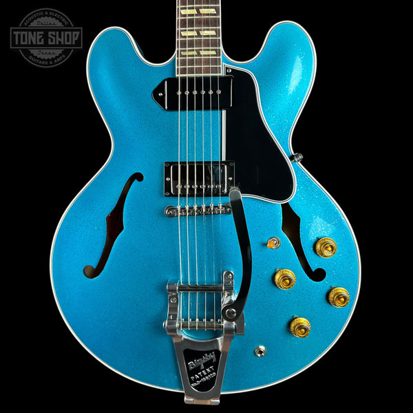 A bright blue glitter electric guitar with a black pickguard, chrome hardware, and gold control knobs, shown against a black background with a Tone Shop watermark in the top left corner.