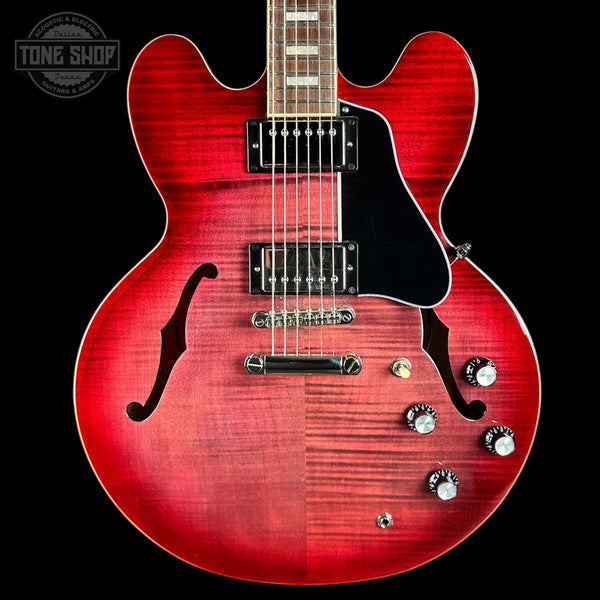 Red electric guitar with a black pickguard on a black background, featuring the Tone Shop logo.