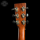 Close-up of the headstock of a wooden acoustic guitar, showing six tuning pegs with decorative gold and silver metal caps, set against a solid black background.