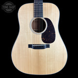A front-facing acoustic guitar with a natural wood finish and a dark tortoiseshell pickguard, shown against a solid black background with a Tone Shop logo in the top-left corner.