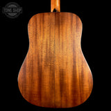 The back of a wooden acoustic guitar, showcasing a rich warm brown grain pattern on a solid black background, with a Tone Shop logo watermark in the top left corner.