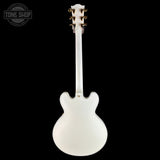 A white electric guitar shown from the back against a solid black background, featuring gold tuning pegs and a Tone Shop watermark in the upper left corner.