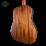 The back of an acoustic guitar with a rich, warm brown wood finish and visible grain patterns, shown against a solid black background with a Tone Shop watermark in the top left corner.