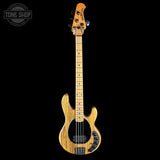 A natural wood bass guitar with a black pickguard and control knobs, shown vertically against a solid black background. A Tone Shop logo is visible in the top-left corner.