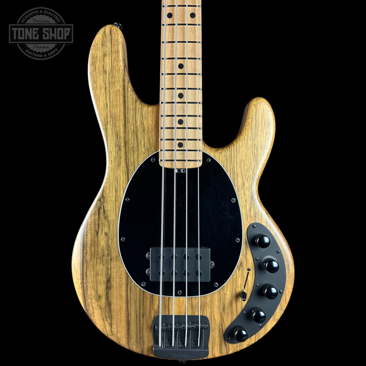 A natural wood four-string bass guitar with a black pickguard and control knobs, shown against a solid black background with a Tone Shop watermark in the top left corner.