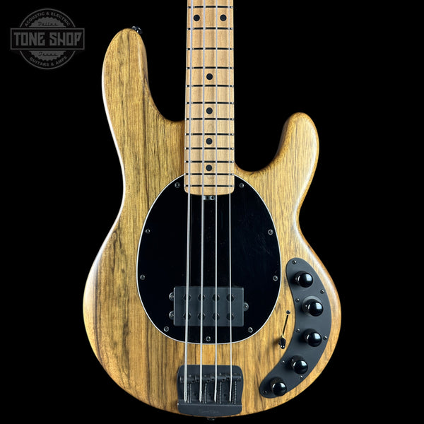 A natural wood four-string bass guitar with a black pickguard and control knobs, shown against a solid black background with a Tone Shop watermark in the top left corner.