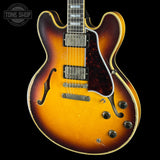 A double-cutaway electric guitar with a classic sunburst finish, featuring a yellow-orange center, dark brown outer edges, and a dark tortoiseshell pickguard. The guitar is photographed against a solid black background with a Tone Shop watermark in the upper left corner.