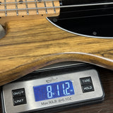 Close-up of a wooden bass guitar body resting on a digital scale displaying 8.12 lbs.