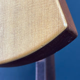 Close-up of a wooden object corner showing a light natural wood grain face and a dark brown edge, photographed against a solid blue background.
