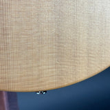 Close-up of a light natural wood grain surface, likely part of a guitar body, with a small metallic screw visible at the bottom against a dark blue background.