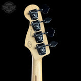 Close-up of the headstock of a bass guitar with four black four-leaf tuning pegs and a light natural wood neck, shown against a solid black background.