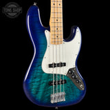 A Fender Strat-style bass guitar with a vibrant blue to green flame finish, a white pickguard, and a maple neck, shown against a black background with a Tone Shop watermark in the top left.