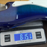 Close-up of a blue-to-teal gradient electric guitar body resting on a digital kitchen scale displaying 8.151 lbs.