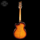 The back of a wooden acoustic guitar with a vibrant sunburst finish, shown against a solid black background with a Tone Shop watermark in the top left corner.