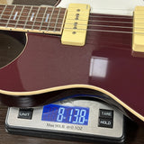 A close-up of a burgundy electric guitar resting on a digital scale showing its weight of 8.138 lbs.