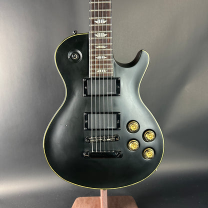 Black electric guitar with gold hardware on a gray background
