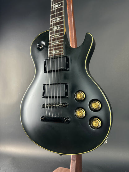 Black electric guitar with gold hardware on a gray background