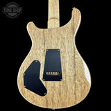 Wooden electric guitar body with black pickguard on a black background, featuring 'Tone Shop' logo.