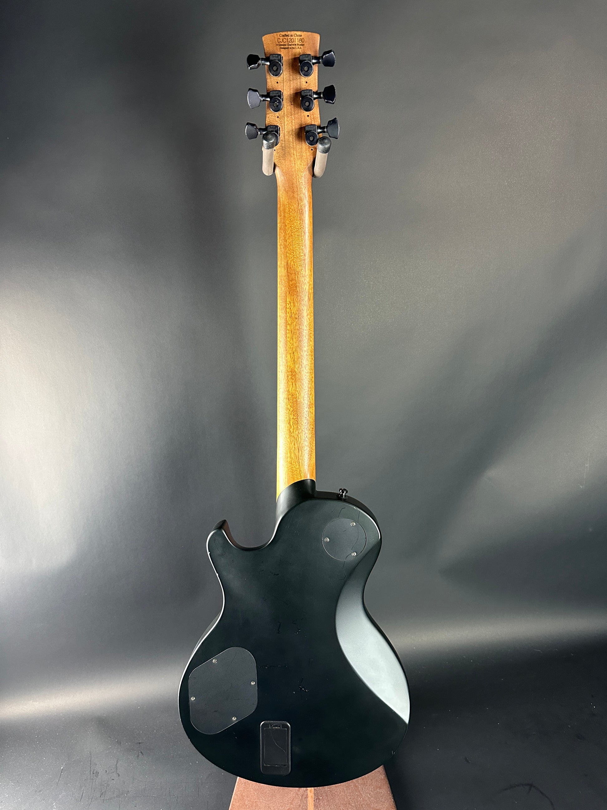 Black electric guitar with wooden neck on a gray background