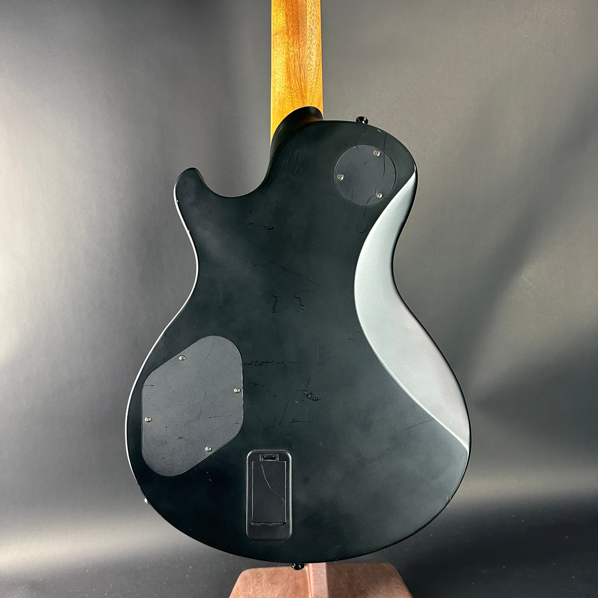 Black electric guitar with a wooden neck on a gray background