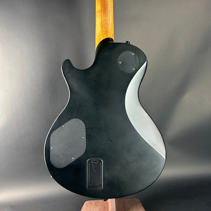 Black electric guitar with a wooden neck on a gray background