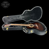 An acoustic guitar with a dark brown wooden body and light-colored neck, resting inside an open black hard guitar case on a solid black background. A 'TONE SHOP' watermark is visible in the top-left corner.