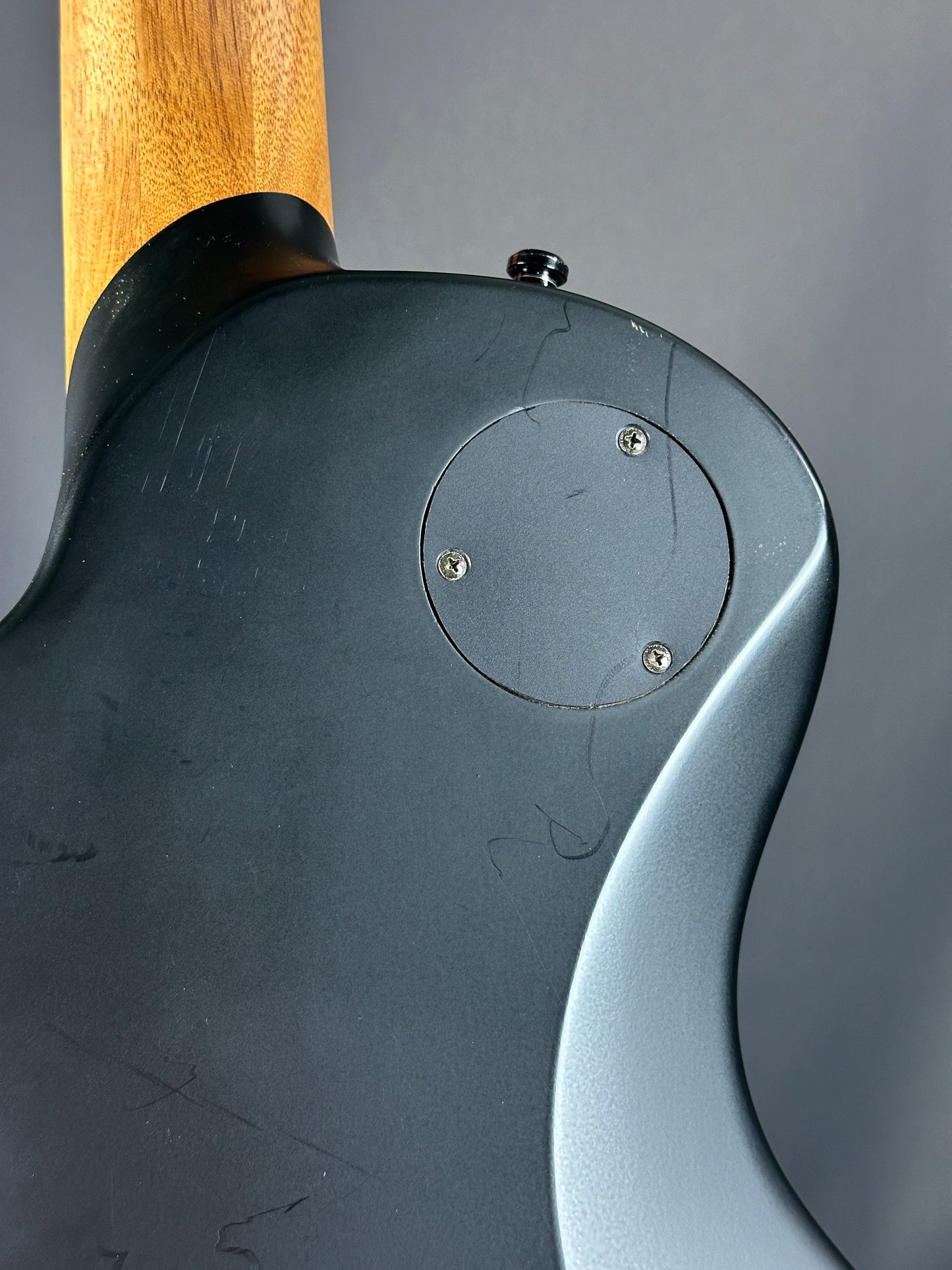 Close-up of a guitar with a wooden neck and dark body against a gray background