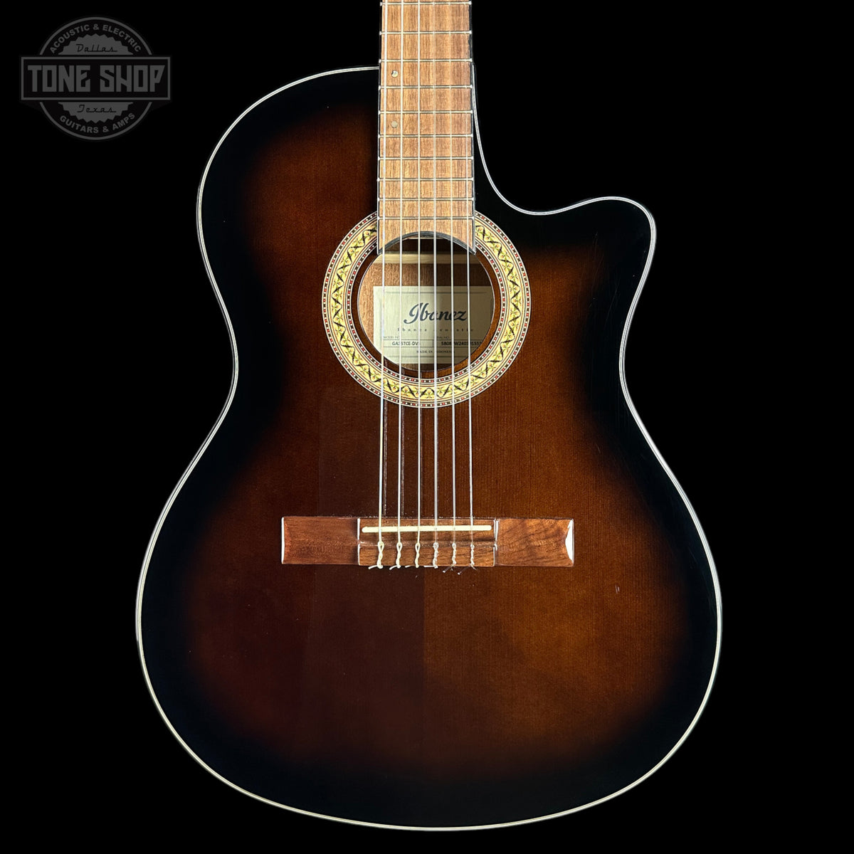An acoustic guitar with a dark brown sunburst finish, featuring a cutaway body, white binding, and a visible Ibanez logo on the soundboard, set against a solid black background.