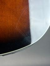 Close-up of a sunburst acoustic guitar body corner, showing the dark center, warm brown outer wood, and a reflective silver metal edge.