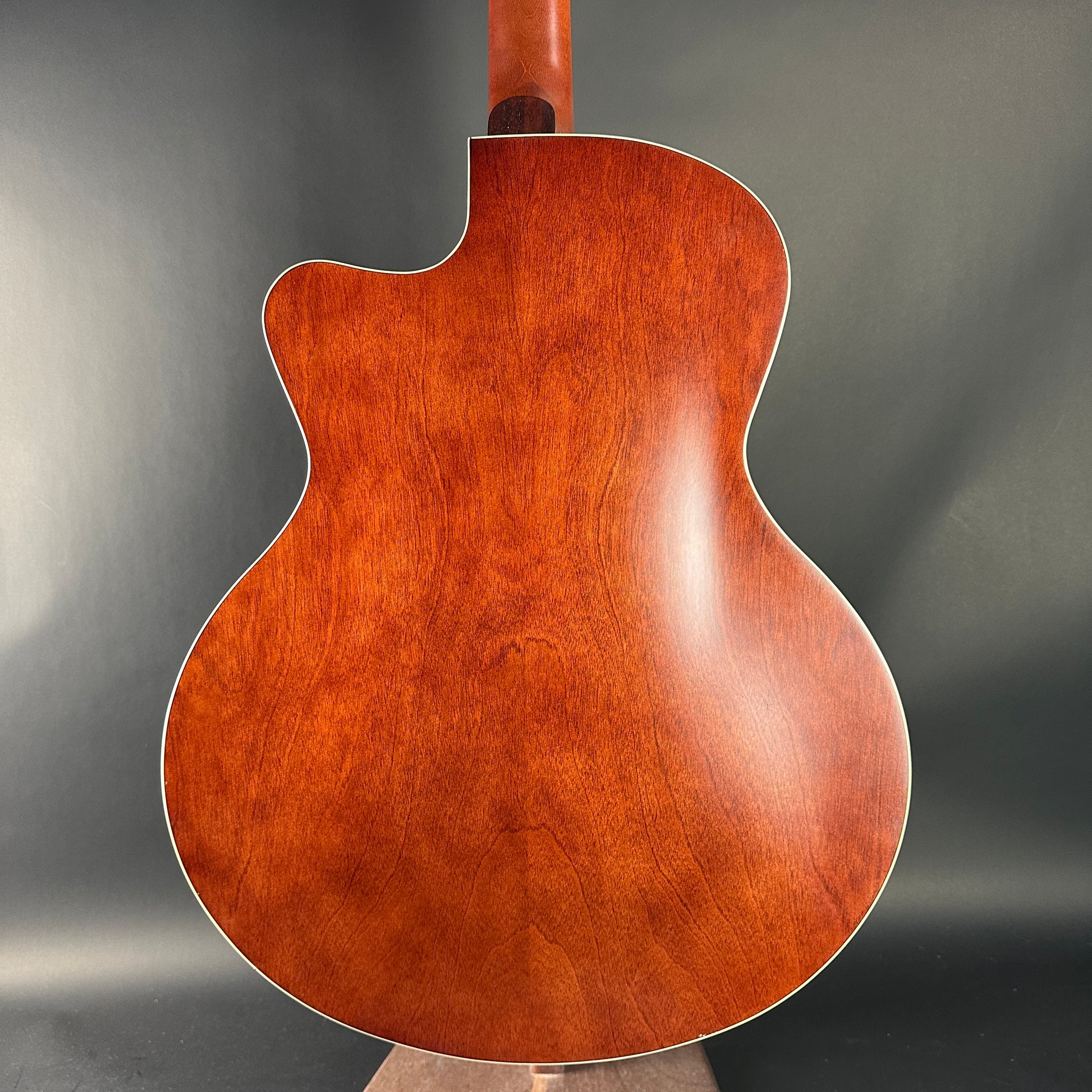 Back view of a wooden acoustic guitar on a gray background