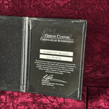 A black Gibson Custom Certificate of Authenticity insert for a Modern DC Standard electric guitar, displayed inside an open black case on a textured dark red velvet background.