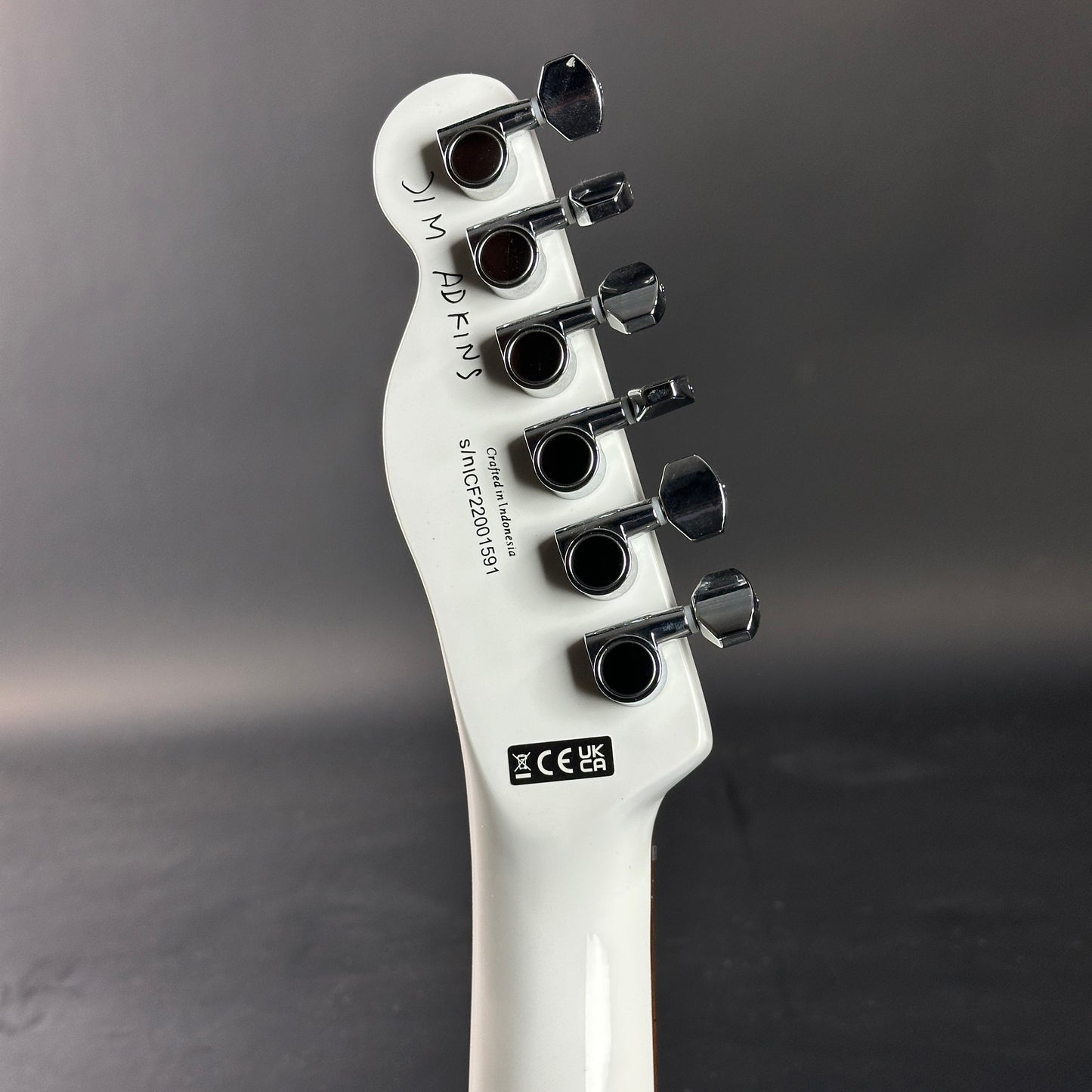 Close-up of a white guitar headstock with tuning pegs on a dark gray background