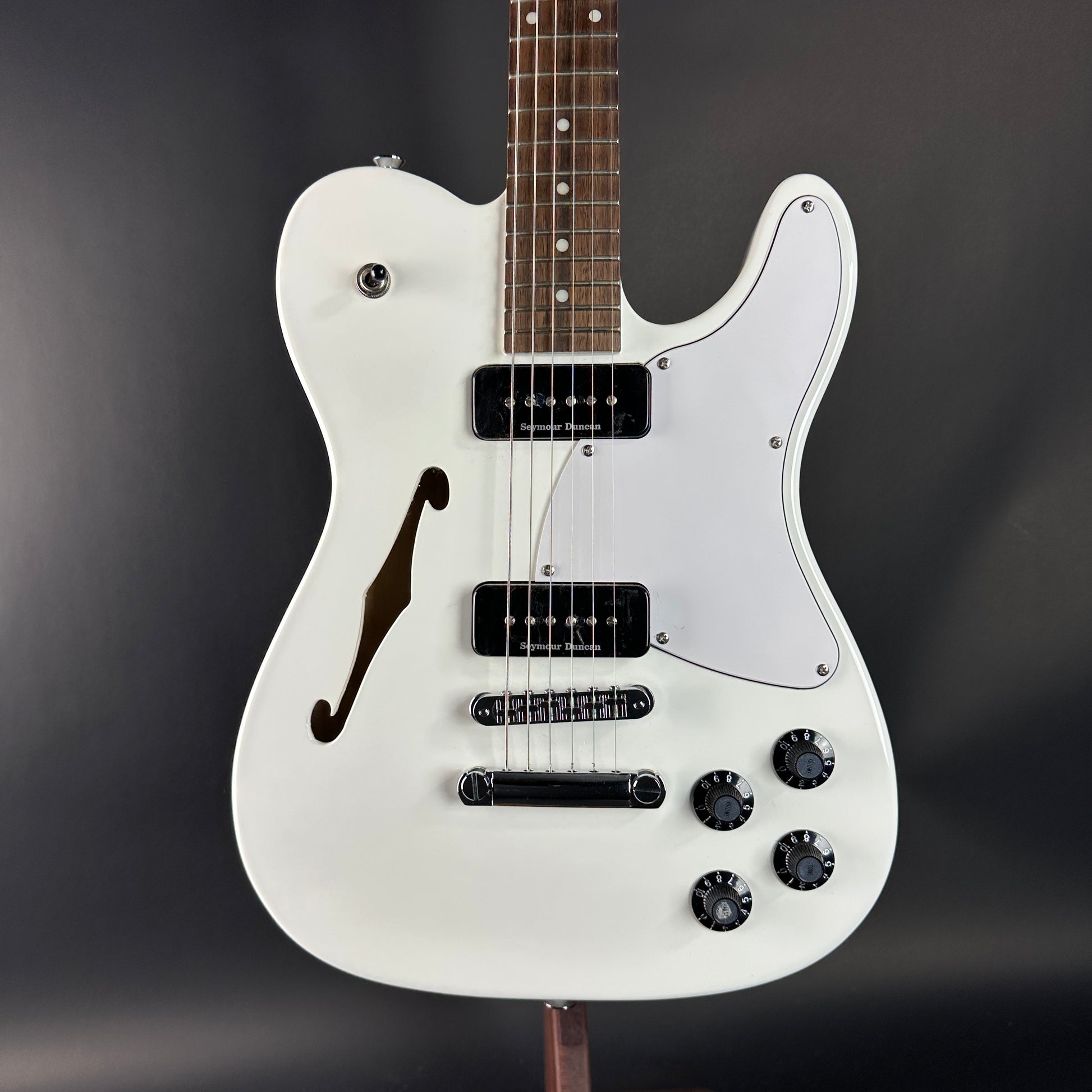 White electric guitar with a dark brown neck on a black background