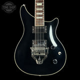 A black electric guitar with a glossy black finish, white binding, and chrome hardware, shown against a solid black background with a Tone Shop watermark in the top-left corner.