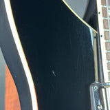 Close-up of a black electric guitar body with a cream binding edge and part of the fretboard visible, showing some surface scratches on the glossy finish.