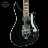 A black electric guitar with a glossy finish, cream edge trim, and a chrome double-cutlass tremolo system, shown against a solid black background with a Tone Shop watermark in the top-left corner.