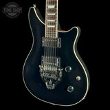 A black electric guitar with a glossy finish, cream binding, and chrome hardware, shown against a solid black background. A Tone Shop watermark is visible in the top-left corner.