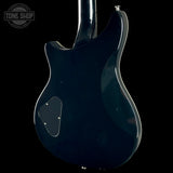 Close-up rear view of an electric guitar body in a glossy dark blue finish, photographed against a black background. A circular Tone Shop watermark is visible in the upper left corner.