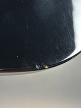 Close-up of a glossy black curved surface with visible scratches and a small orange speck near the edge, set against a light gray background.